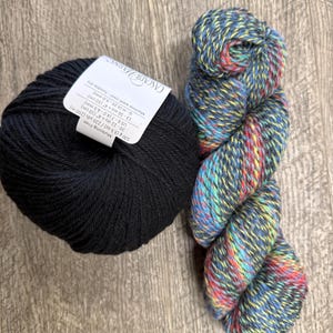 May include: Two skeins of yarn. One is a tightly wound ball of black yarn with a white label. The other is a twisted skein of multicolored yarn with blue, red, yellow, and green hues. The label on the black yarn reads "CASCADE YARNS".
