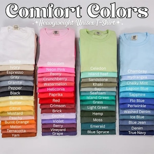 Op de afbeelding: Een kaart met 36 verschillende kleuren t-shirts, met de tekst "Comfort Colors Heavyweight Unisex T-Shirt" bovenaan. De kleuren zijn gerangschikt in drie kolommen, waarbij elke kolom een ​​andere kleurenfamilie vertegenwoordigt: wit, roze, groen, blauw.