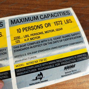May include: A rectangular boat capacity decal featuring black text on yellow and silver backgrounds. It states MAXIMUM CAPACITIES, 10 PERSONS OR 1572 LBS, 2250 LBS PERSONS MOTOR GEAR, 125 H.P. MOTOR, NITRO NX 750 SC, and includes NMMA and BIA logos.