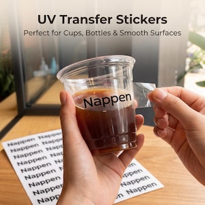 May include: A clear plastic cup containing a dark liquid, possibly coffee, with the word "Nappen" printed on it. A UV transfer sticker is being peeled off the cup. The image also shows the text "UV Transfer Stickers" and "Perfect for Cups, Bottles & Smooth Surfaces."