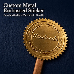 Puede incluir: Una pegatina circular de metal dorado en relieve con un borde dentado, que presenta la palabra Handmade en el centro y repetida alrededor del círculo interior. El texto Custom Metal Embossed Sticker Premium Quality Waterproof Durable es visible.