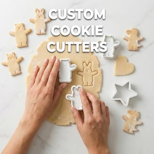 May include: The image shows the words "CUSTOM COOKIE CUTTERS" in white block letters. There are several animal-shaped cookie cutters and cookies, including a bear, bunny, cat, and alligator. The cookie dough is in the center, and hands are using the cutters.
