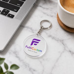 Op de afbeelding: Een ronde sleutelhanger van helder acryl met een paars gestileerd letter F-logo boven de tekst FulliCustom en de zin Make It Yours in een meerkleurig lettertype. De sleutelhanger is voorzien van een zilverkleurige metalen ring en een korte ketting.