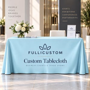 以下が含まれることがあります： FULLICUSTOM、Custom Tablecloth、BUSINESS EVENTS & TRADE SHOWSという濃い青色のロゴとテキストがプリントされた水色の長方形のテーブルクロス。テーブルの上には、白い花が入ったガラスの花瓶と小さな看板スタンドが置かれています。