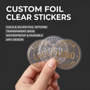 Może przedstawiać: Przezroczyste, okrągłe naklejki ze złotymi akcentami foliowymi są trzymane na ciemnym tle. Naklejki zawierają tekst "LOGO STICKER" i "CUSTOM" w okrągłym wzorze. Tekst "CUSTOM FOIL CLEAR STICKERS" znajduje się na górze.