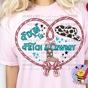 Puede incluir: Camiseta rosa con un diseño gráfico de un corazón de lazo con un sombrero de vaquero, botas y el texto "Fixin' to Fetch a Cowboy".