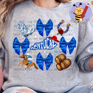 May include: A gray sweatshirt with a blue and white design featuring a horse and jockey, a horseshoe, a red hat, barrels, and the word "Kentucky". The design is surrounded by blue bows.