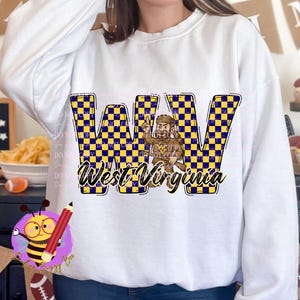 May include: White sweatshirt featuring a WV graphic with a blue and yellow checkered pattern. The graphic includes a cartoon figure and the words "West Virginia". The sweatshirt is a casual, comfortable garment.