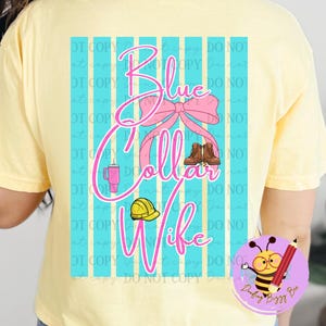 May include: A light yellow t-shirt with a graphic on the back that says "Blue Collar Wife" in pink script. The graphic includes a pink bow, work boots, a coffee cup, and a yellow hard hat. The background has blue and white stripes.