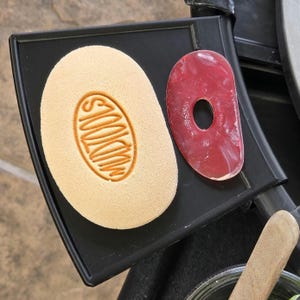 Puede incluir: Una herramienta de parrilla negra con un difusor de calor de cerámica rojo y blanco y un difusor de calor beige con la palabra "Smokin" impresa.