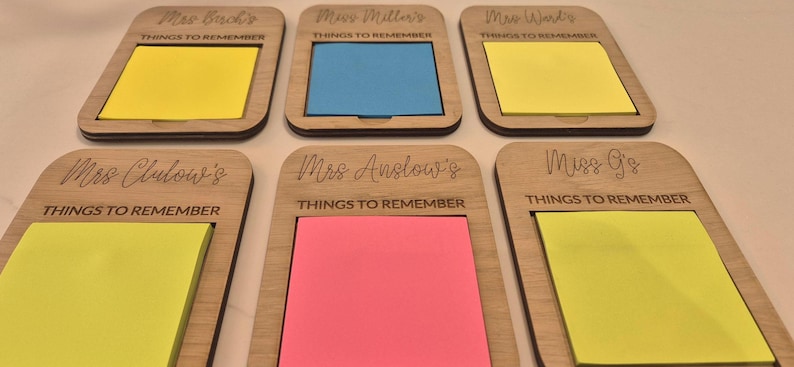 May include: Six wooden memo holders with colorful sticky notes. Each holder has a name engraved at the top and the words "THINGS TO REMEMBER" below. The sticky notes are yellow, blue, and pink.