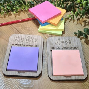 May include: Two rectangular wooden holders for sticky notes, each featuring a cutout for a square pad. One holder is engraved with "Mrs Gill's THINGS TO REMEMBER" and holds a purple pad, while the other says "Amy's THINGS TO REMEMBER" with a peach pad.