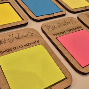 May include: Wooden memo holders with colorful sticky notes. Each holder has a rectangular frame with rounded corners and a slot for the notes. The holders are engraved with the words "THINGS TO REMEMBER" and names like "Mrs. Clulow's" and "Mrs. Anelor's".