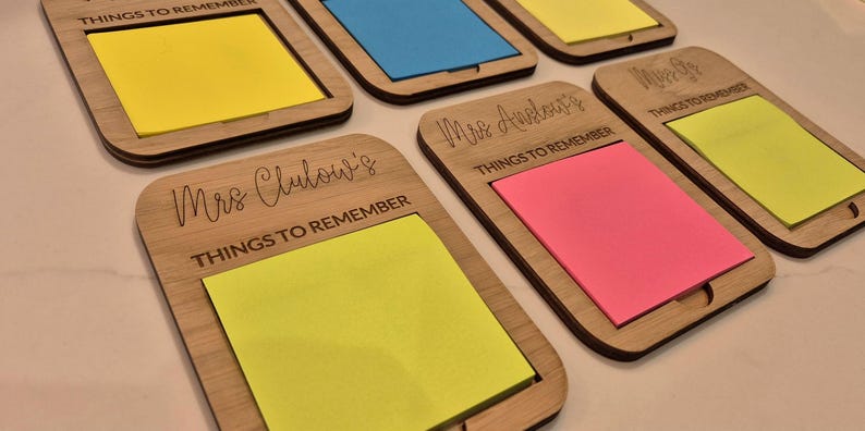 May include: Wooden memo holders with colorful sticky notes. Each holder has a rectangular frame with rounded corners and a slot for the notes. The holders are engraved with the words "THINGS TO REMEMBER" and names like "Mrs. Clulow's" and "Mrs. Anelor's".
