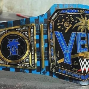 May include: A custom wrestling championship belt with a black and blue design. The belt features gold accents, the word "YEEET" in blue, and the WWE logo. The side plates have a palm tree design.