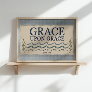 May include: A rectangular framed wall art piece featuring a light beige fabric background with a blue gingham border. The text reads GRACE UPON GRACE and John 1:16 in dark blue. Below the text are three wavy lines and two green leaf sprigs.