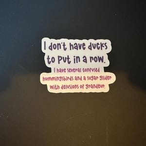 May include: A white sticker with purple and pink text that reads "I don't have ducks to put in a row. I have several confused hummingbirds and a sugar glider with delusions of grandeur."