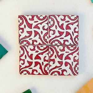 Może przedstawiać: Cztery kwadratowe płytki ceramiczne z białym tłem i czerwonym wzorem kwiatowym. Płytki są ułożone w kwadrat.
