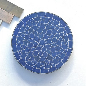 May include: A blue and white ceramic tile coaster with a geometric pattern. The coaster is round and has a white border.