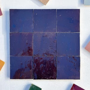 Puede incluir: Nueve azulejos de cerámica cuadrados de color azul índigo oscuro con una ligera variación de tono. Los azulejos están dispuestos en una cuadrícula de 3x3.