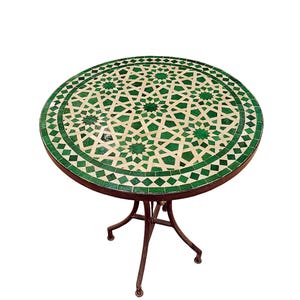 May include: A round outdoor table with a mosaic tile top. The tabletop features a geometric pattern in shades of green and cream. The table has a dark metal frame and three legs.
