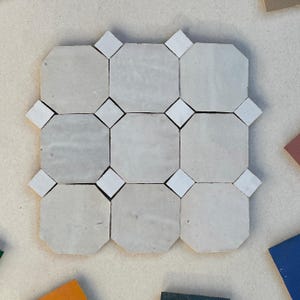 Peut inclure: Gros plan sur un assemblage de neuf carreaux octogonaux gris clair, avec des inserts en forme de losange blancs. Les carreaux sont disposés en grille, créant un motif géométrique. L'ensemble est de couleur neutre.