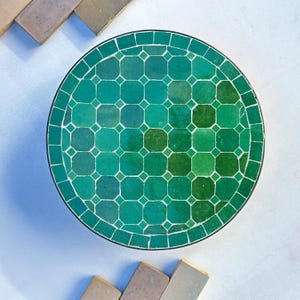 Puede incluir: Una mesa redonda de mosaico verde con un patrón geométrico. La mesa está hecha de pequeñas baldosas cuadradas.