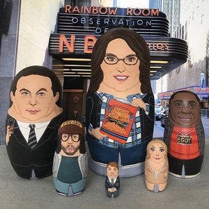 Puede incluir: Un conjunto de seis muñecas rusas de madera pintadas a mano, o muñecas matrioska, que representan personajes del programa de televisión "30 Rock". La muñeca más grande representa al personaje de Liz Lemon, sosteniendo un libro titulado "Lemon: La autobiografía de una mujer que fue a la universidad". Las otras muñecas representan a los personajes de Jack Donaghy, Kenneth Parcell, Frank, Jenna Maroney y Tracy Jordan.