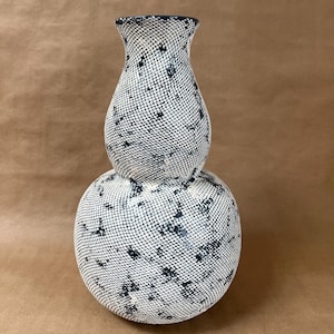 May include: A ceramic vase with a unique design. The vase is composed of two stacked, rounded sections. The surface is covered in a white, net-like pattern with dark blue accents. The top opening is dark blue.