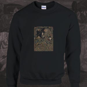 Könnte beinhalten: Ein schwarzes Langarm-Sweatshirt mit Rundhalsausschnitt und einem zentralen Grafikdruck. Die Illustration zeigt eine Kriegerfigur, die einer großen, monströsen Kreatur gegenübersteht, in detaillierter Linienführung mit keltischen Knotenmustern.
