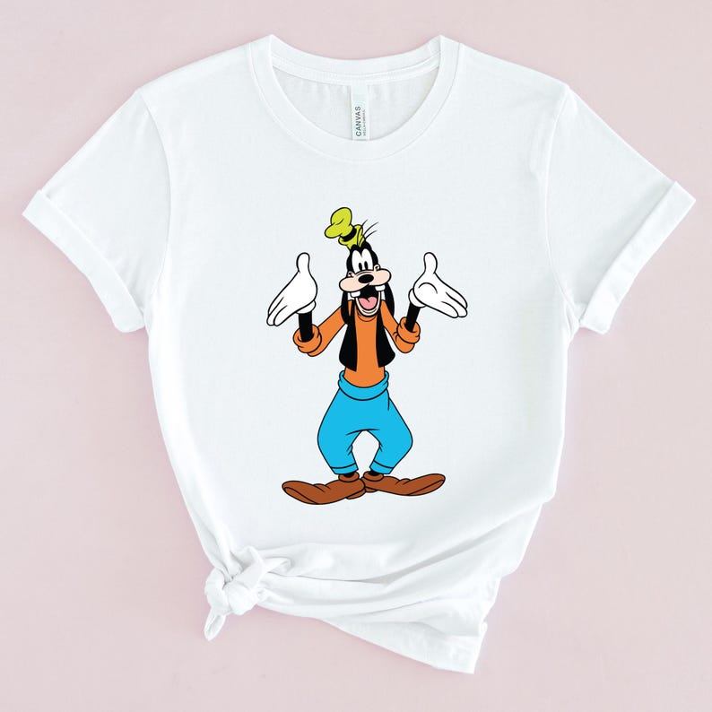 May include: White t-shirt with a cartoon image of Goofy, a Disney character, with his arms outstretched. Goofy is wearing a yellow hat, orange shirt, blue pants, and brown shoes.