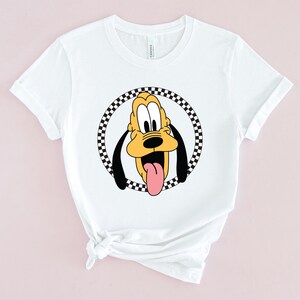 Op de afbeelding: Wit T-shirt met een zwart-wit geblokte cirkel rond een cartoon afbeelding van Pluto, een gele hond met zwarte oren en een rode tong die uitsteekt.