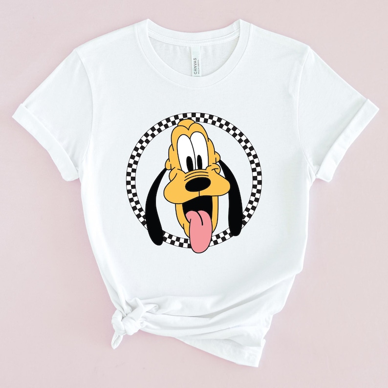 Op de afbeelding: Wit T-shirt met een zwart-wit geblokte cirkel rond een cartoon afbeelding van Pluto, een gele hond met zwarte oren en een rode tong die uitsteekt.