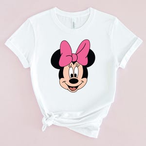 Peut inclure: T-shirt blanc avec une image de dessin anim&eacute; de Minnie Mouse avec un n&oelig;ud rose.