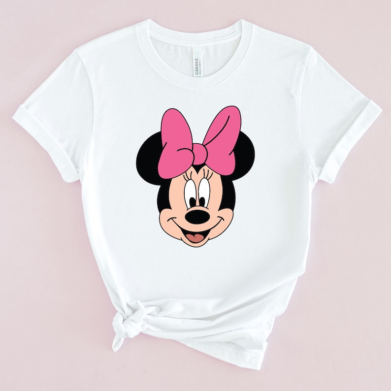 Peut inclure: T-shirt blanc avec une image de dessin anim&eacute; de Minnie Mouse avec un n&oelig;ud rose.