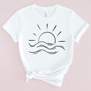 May include: White t-shirt with a black line drawing of a sun setting over waves.