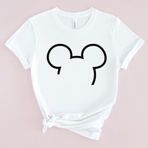 Puede incluir: Camiseta blanca con un contorno negro de las orejas de Mickey Mouse.