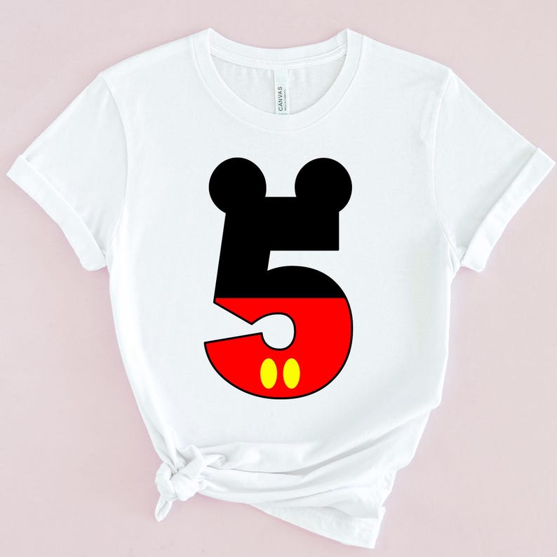May include: White t-shirt featuring a large number 5 in the style of a famous cartoon character. The top of the number is black with two circular shapes, the bottom is red with two yellow circles.