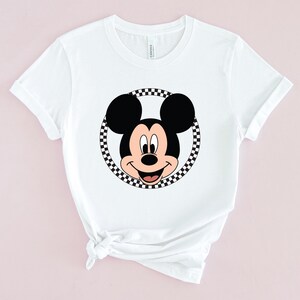 Op de afbeelding: Wit T-shirt met een zwart-wit geblokte cirkel rond een cartoon afbeelding van Mickey Mouse.