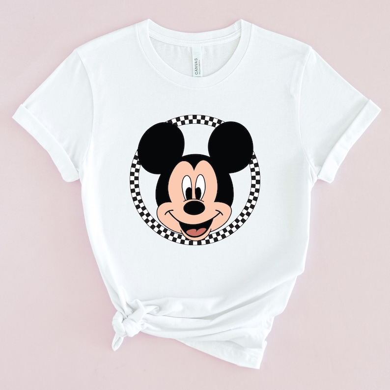 Op de afbeelding: Wit T-shirt met een zwart-wit geblokte cirkel rond een cartoon afbeelding van Mickey Mouse.