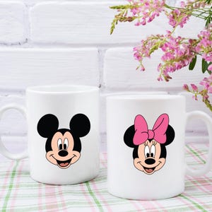 Peut inclure: Deux tasses en c&eacute;ramique blanche avec des images de dessins anim&eacute;s de Mickey Mouse et Minnie Mouse. Mickey Mouse porte un short rouge et des chaussures jaunes. Minnie Mouse porte un n&oelig;ud rose et des chaussures rouges.