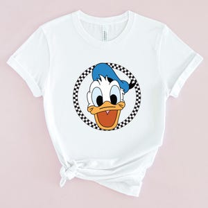 Op de afbeelding: Wit T-shirt met een zwart-wit geblokte cirkel rond een cartoon afbeelding van Donald Duck met een blauwe hoed.