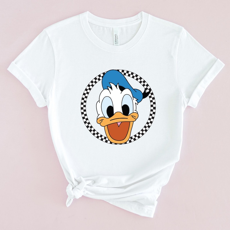 Op de afbeelding: Wit T-shirt met een zwart-wit geblokte cirkel rond een cartoon afbeelding van Donald Duck met een blauwe hoed.