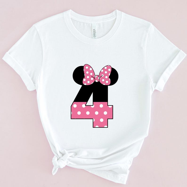 May include: White t-shirt featuring a black and pink graphic. The graphic includes black mouse ears, a pink polka dot bow, and the number 4 in black and pink polka dots. The shirt is made of a soft material.