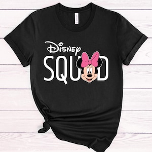 Puede incluir: Camiseta negra con la frase blanca "Disney SQUAD" y un dibujo de Minnie Mouse. Minnie Mouse lleva un lazo rosa. La camiseta tiene las mangas dobladas y un nudo en la parte inferior.
