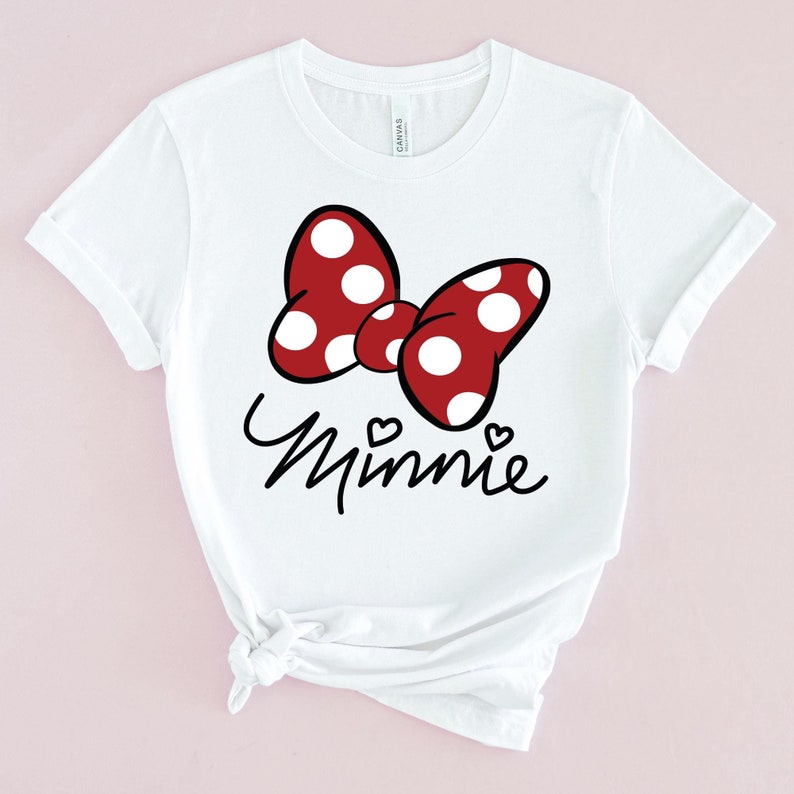 Puede incluir: Camiseta blanca con un lazo rojo y blanco de lunares y la palabra "Minnie" en letra negra.