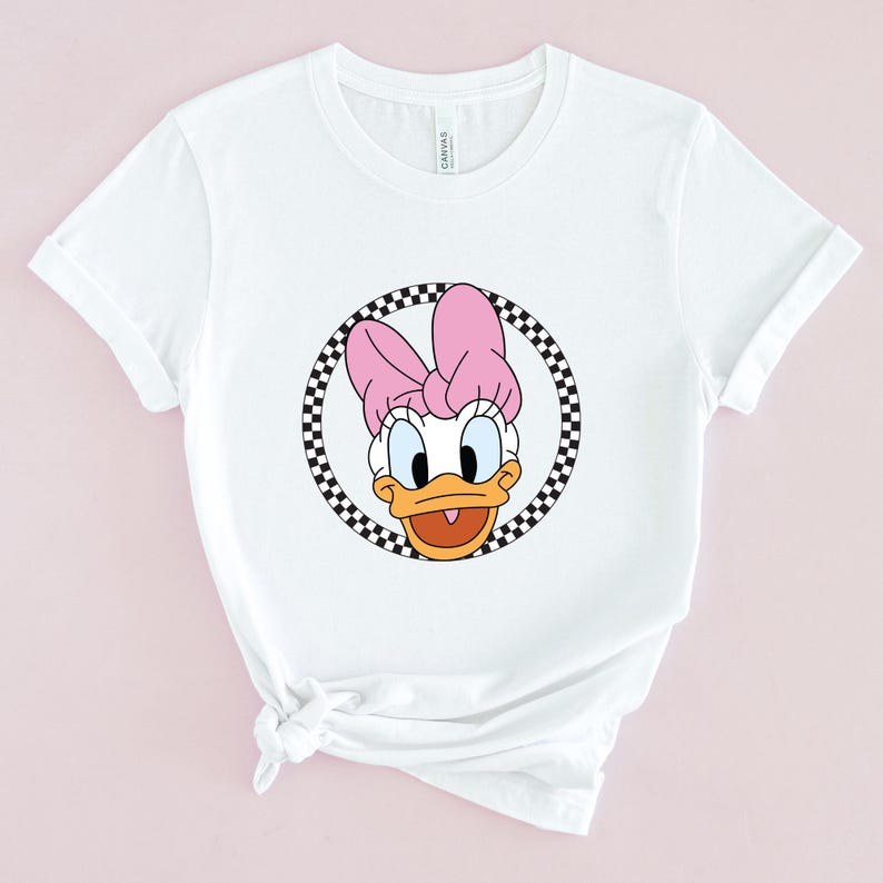 Op de afbeelding: Wit T-shirt met een cartoon afbeelding van Daisy Duck met een roze strik. De afbeelding is omgeven door een zwart-wit geblokte cirkel.