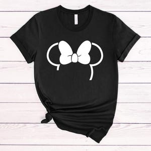 Puede incluir: Camiseta negra con un contorno blanco de las orejas de Mickey Mouse con un lazo en la parte superior.