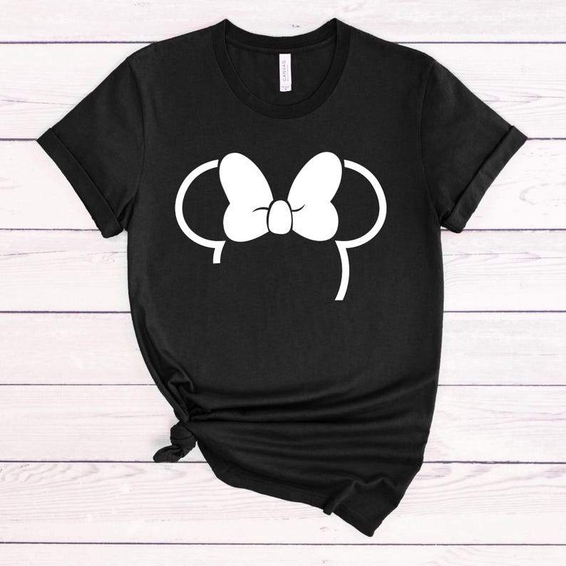 Puede incluir: Camiseta negra con un contorno blanco de las orejas de Mickey Mouse con un lazo en la parte superior.
