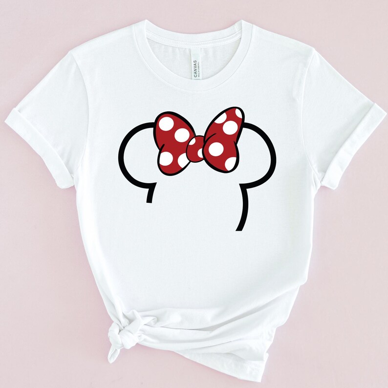 Op de afbeelding: Wit T-shirt met een rode strik met witte stippen en zwarte muizenoren. Het ontwerp staat in het midden van de voorkant van de shirt. Het shirt heeft korte mouwen en een ronde hals.